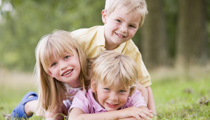 Three young children playing outdoors smiling lying on the grass