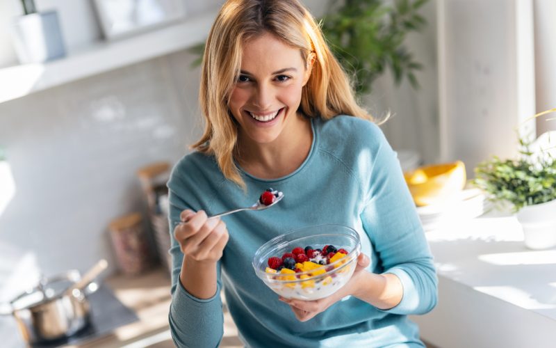 Shot of kind beautiful woman eating a healthy fruit bowl while sitting on the table in the kitchen at home