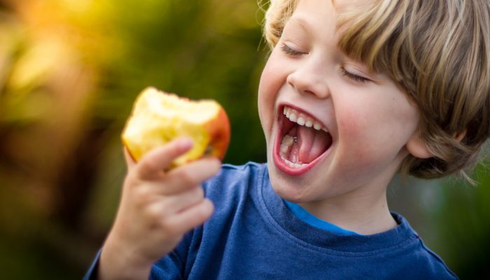 close up of 5 year old blonde child with mouth open about to take a bite of an apple